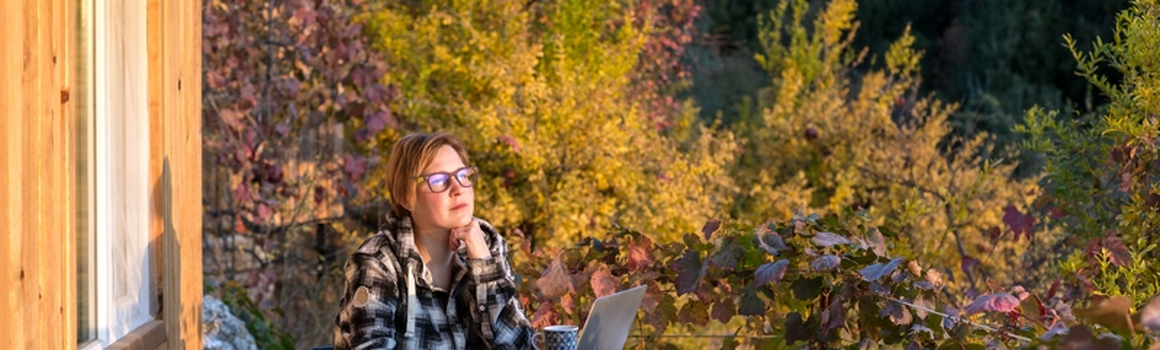 Žena s notebookem sedí na terase před chatou