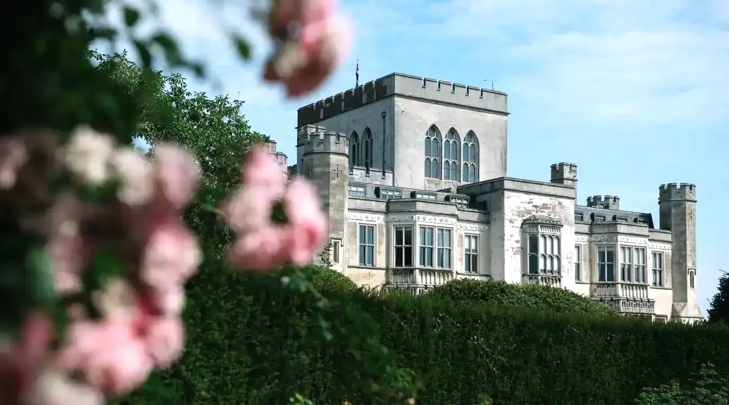 Exterior of Ashridge House looms from behind a row of trees and pink flowers