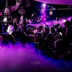 A lively scene at L'Arc Paris nightclub, showcasing a vibrant crowd basking in colorful lights and swirling fog, capturing the essence of an exciting night out.
