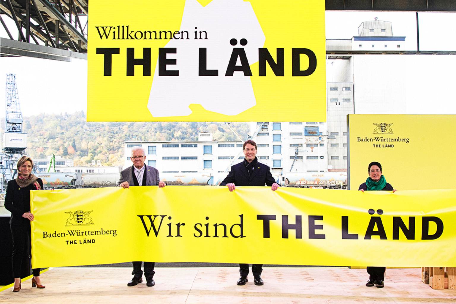 Ministerpräsident Winfried Kretschmann und andere Personen halten einen "Wir sind THE LÄND" Banner hoch.