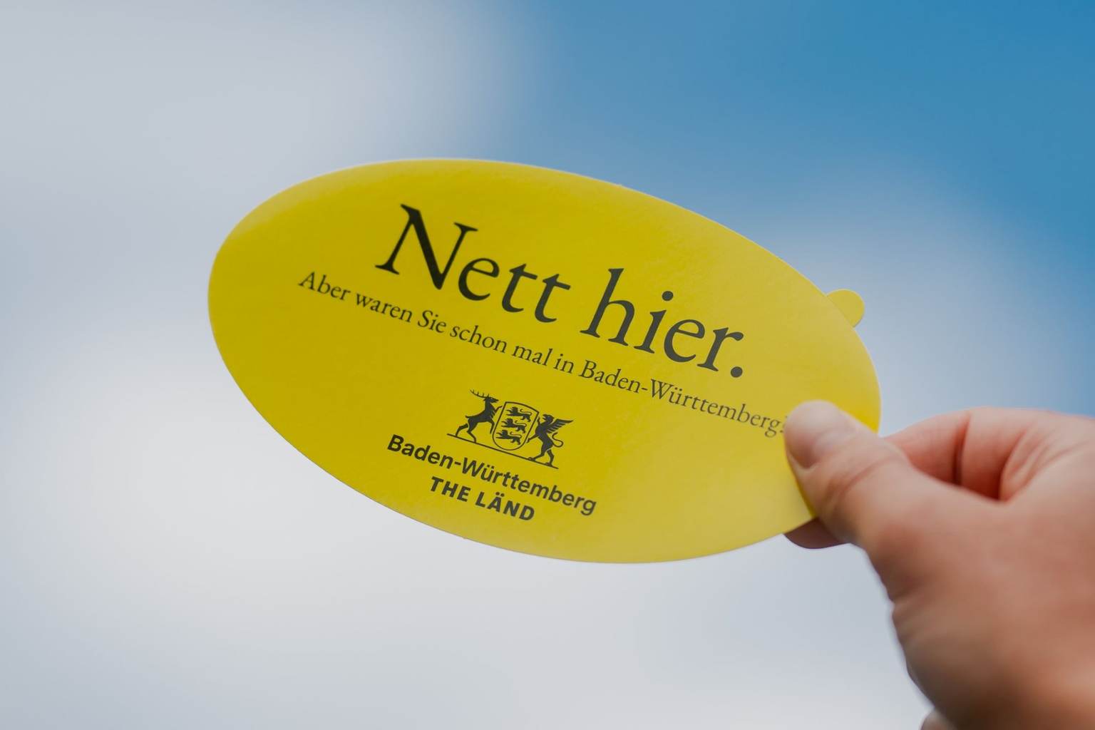 Ein Foto von einem gelben Aufkleber mit der Aufschrift "Nett hier. Aber waren Sie schon mal in Baden-Württemberg?"
