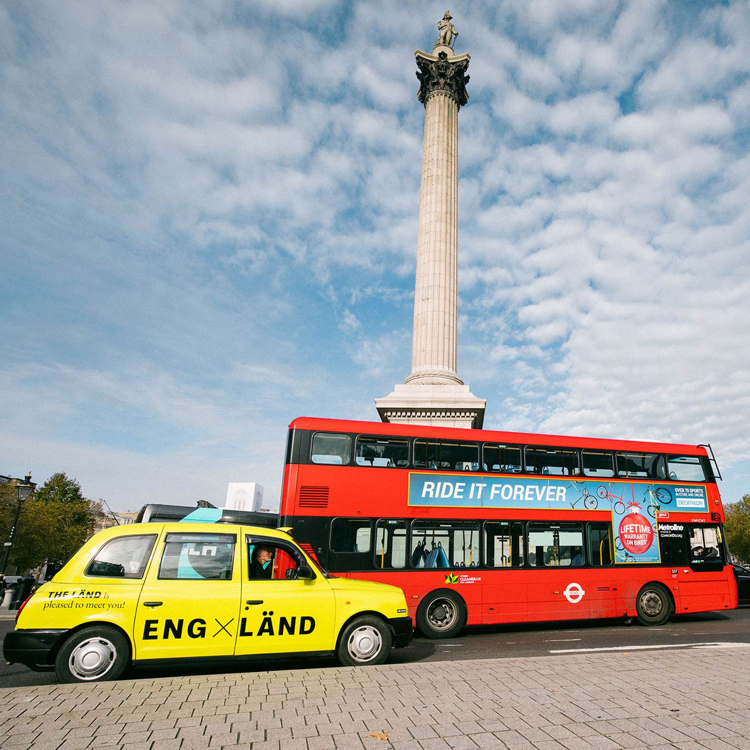 Ein neongelbes Taxi und ein roter Touristen-Bus stehen vor dem Buckingham Palace in England.