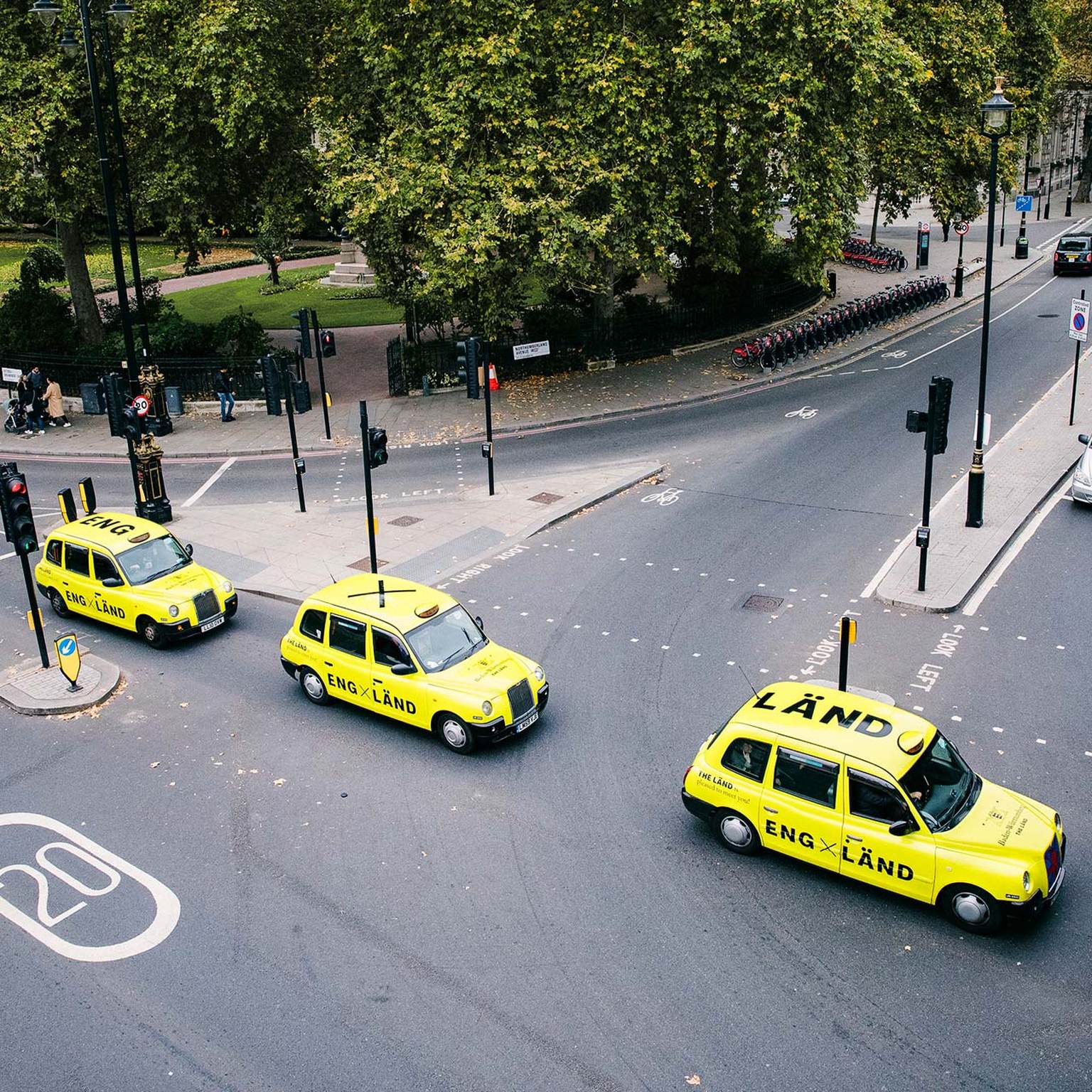 Three neon yellow cabs with "LÄND" lettering are driving through streets of england.