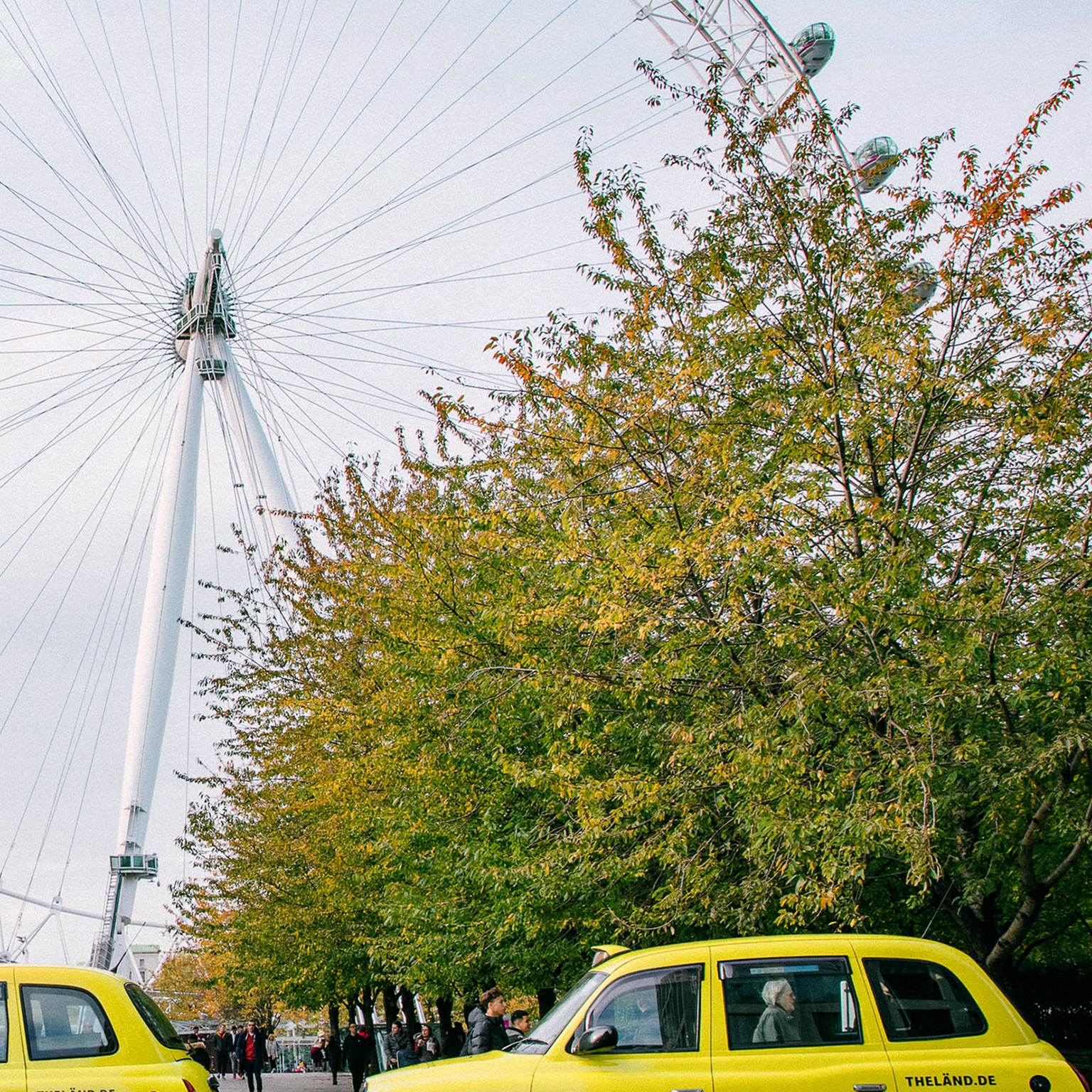 Neon yellow cabs with "LÄND" lettering are standing in front of the London Eye in England.