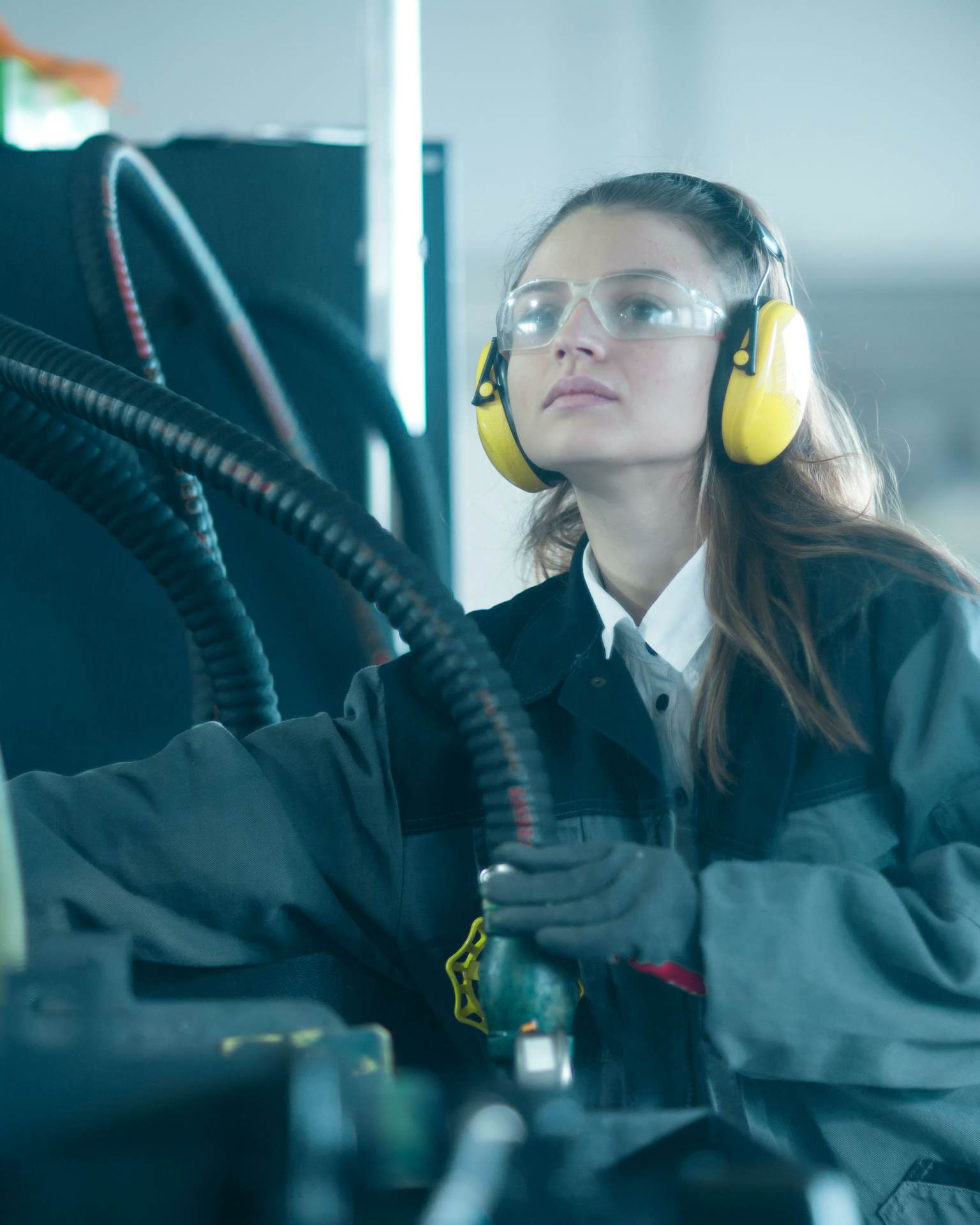 A woman wears hearing protection while working on an industrial machine.