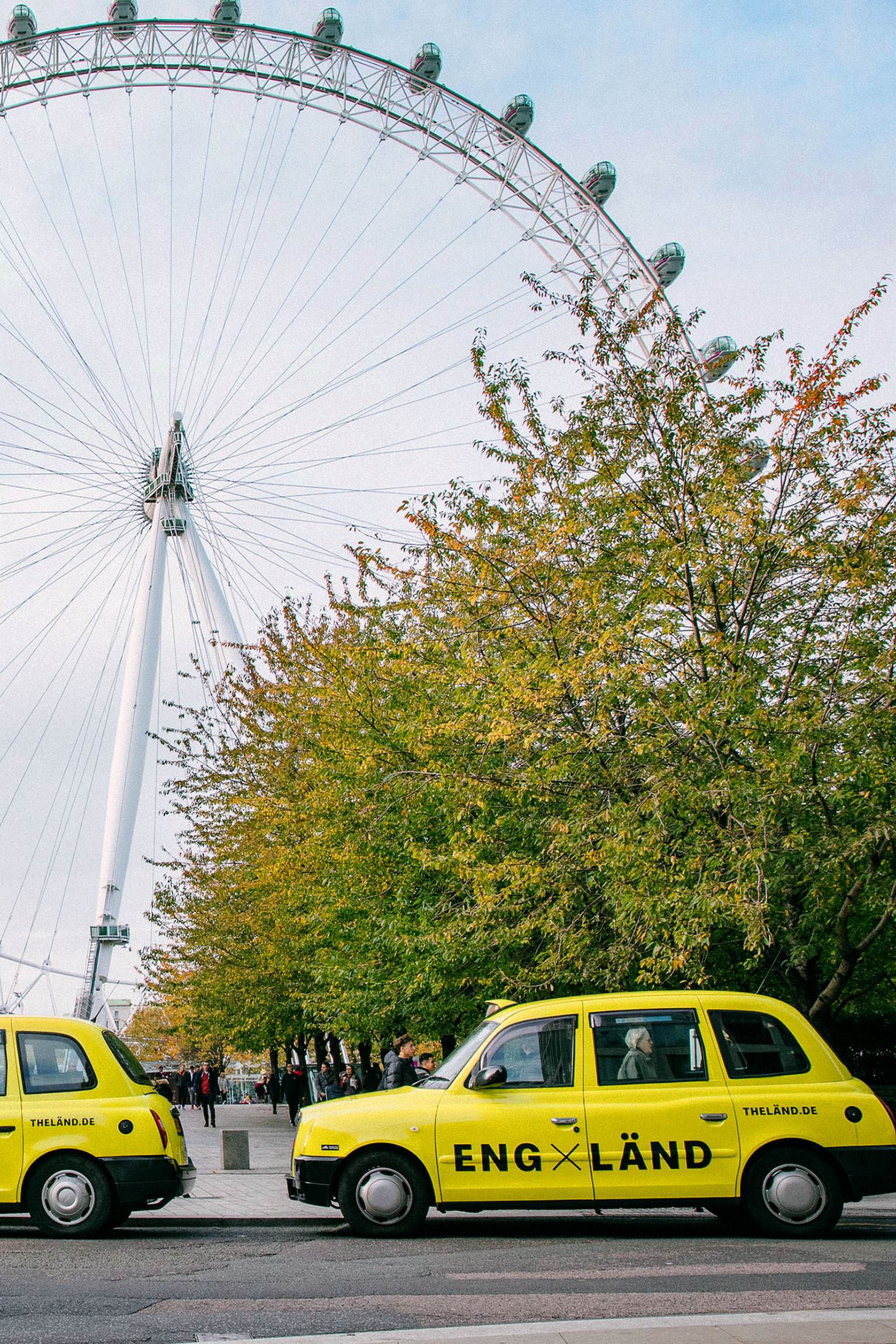 Neongelbe Taxis mit "LÄND" Schriftzügen stehen vor einem Riesenrad in England
