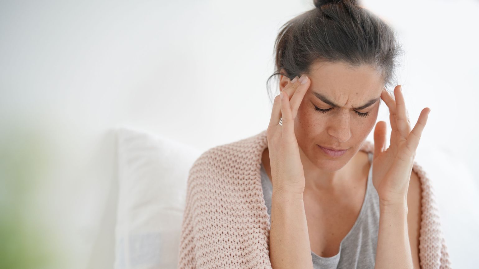 Frau zeigt typischen Verlauf einer Erkältung und fasst sich wegen Kopfschmerzen an die Schläfen