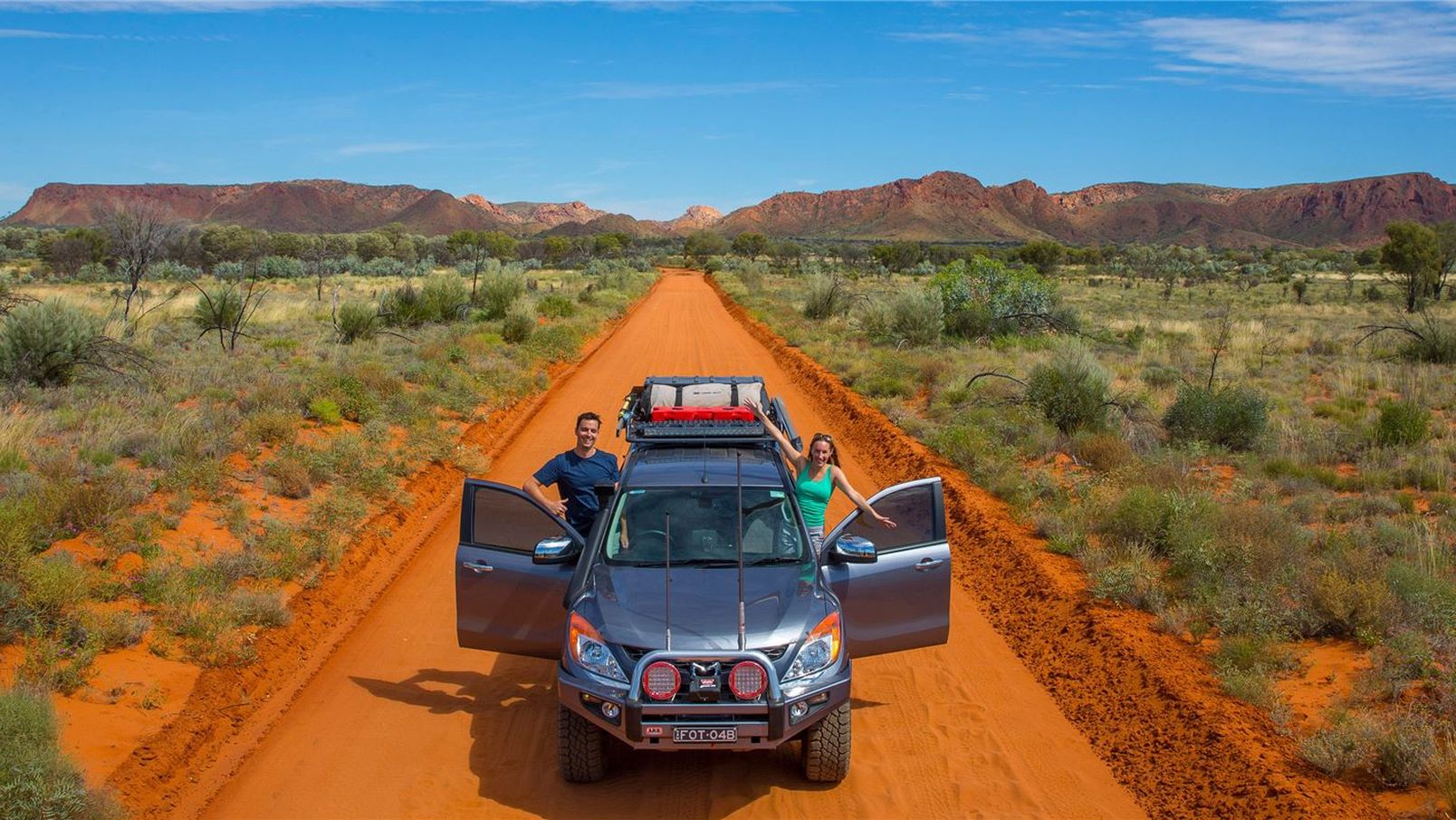 A couple driving a four wheel drive on a red dirt track near Alice Springs