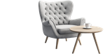 Light gray tufted armchair with wooden legs next to a round light-wood side table holding a white cup and saucer.