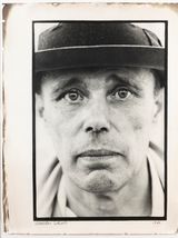 Schwarz-Weiß-Porträt einer Person mit Hut, die mit neutralem Gesichtsausdruck direkt in die Kamera blickt.