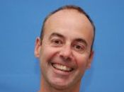A headshot of William with a big smile in front of a blue background.