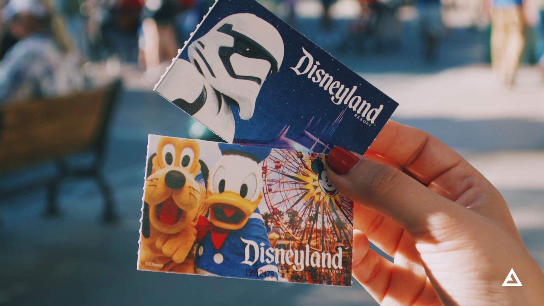 A hand holds a pair of Disneyland Park tickets