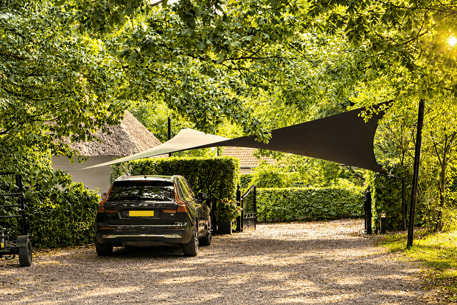 Maatwerk schaduwdoek als carport boven een auto, omringd door groen en bomen.