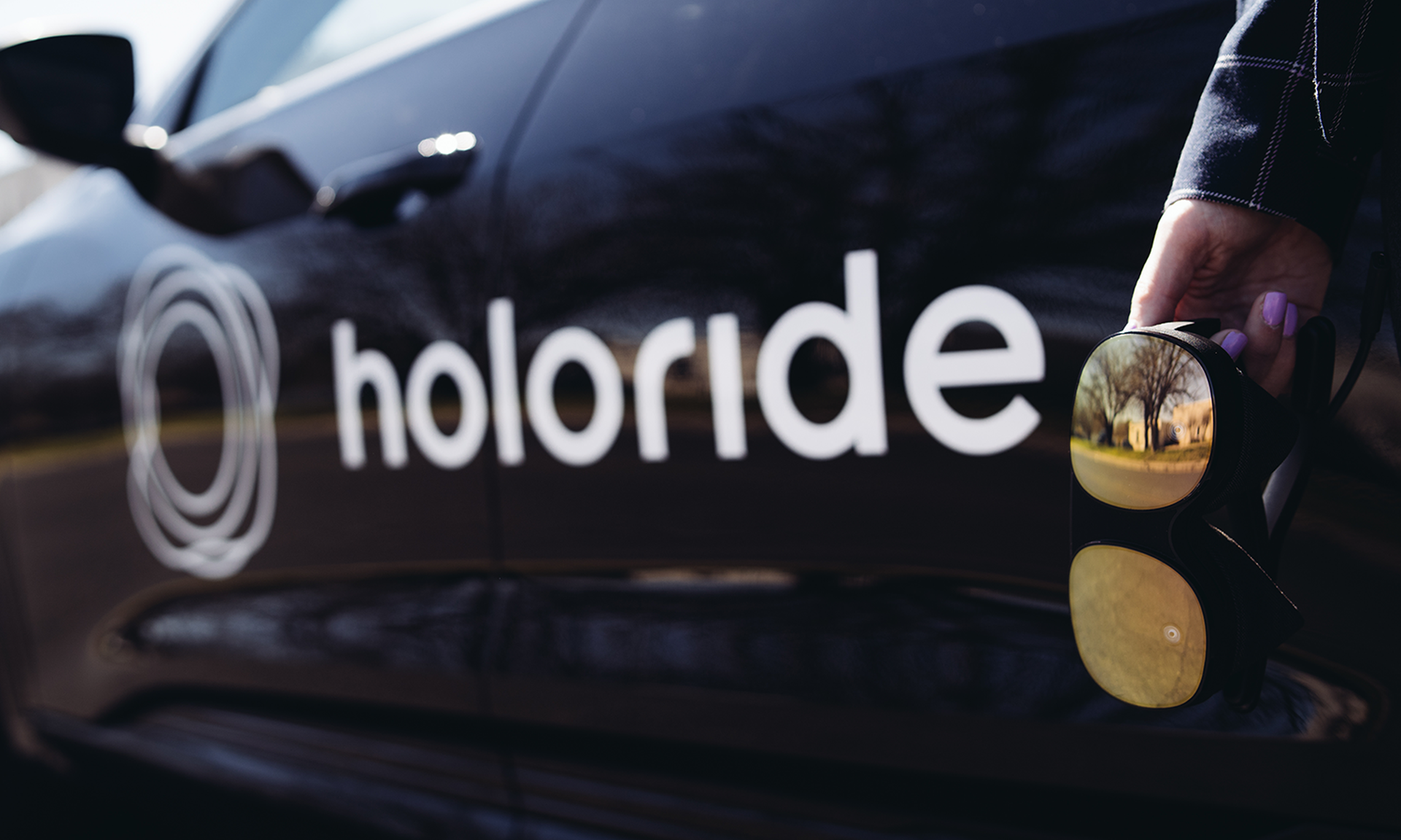 VR headset in the hand of a girl, hanging in front of a car with holoride branding