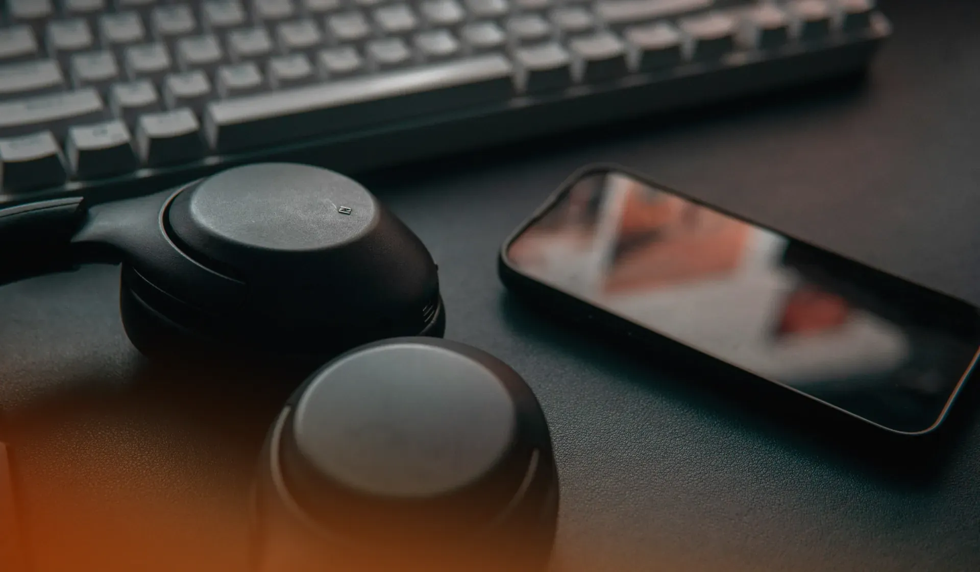 Headphones, smartphone and mechanical keyboard on a desk, the everyday screens where brands are now heard