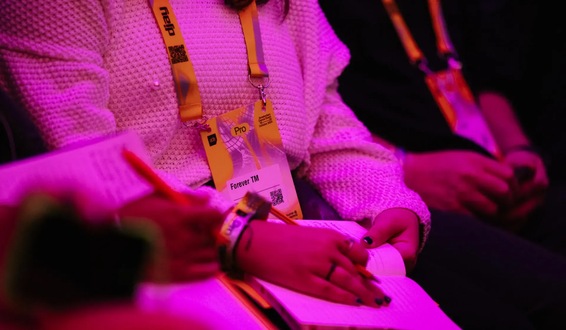 Audience members with lanyards and notebooks under magenta lighting at the ADE panel