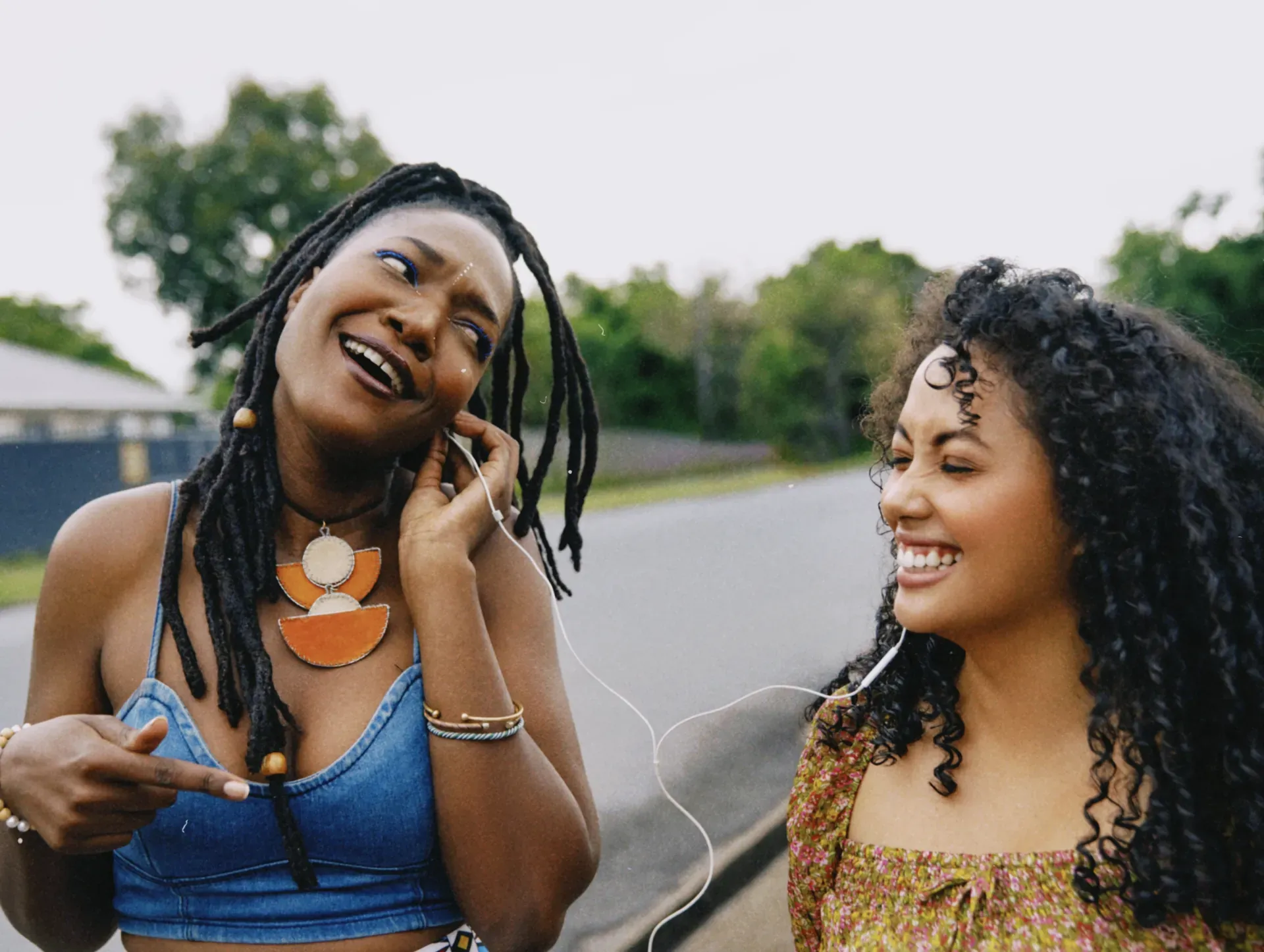 Two friends laughing as they share a pair of earphones, music moving between people rather than playing for one