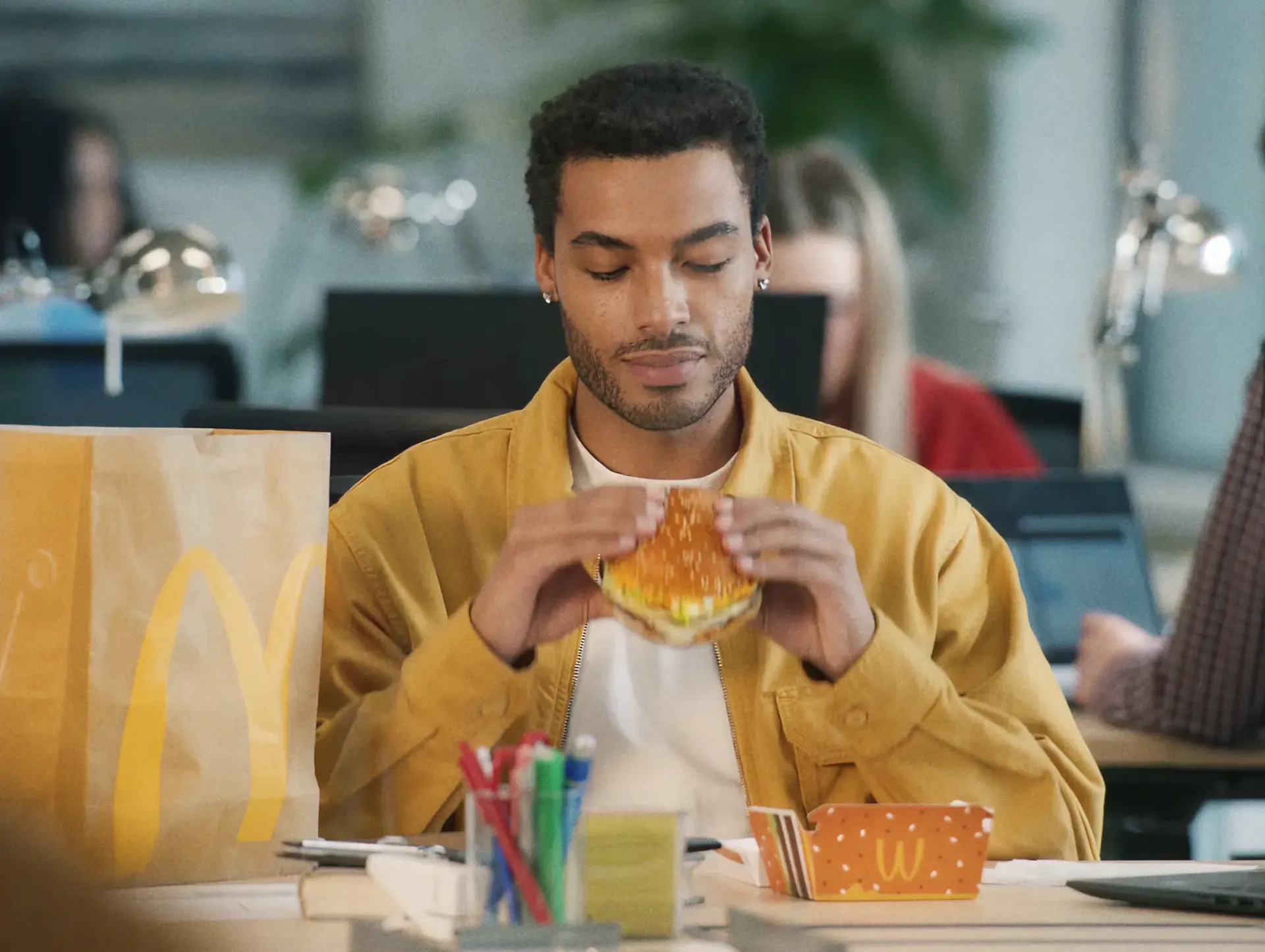 Man in a yellow jacket eating a burger and holding McDonald's fries, from the Sound of McDonald's