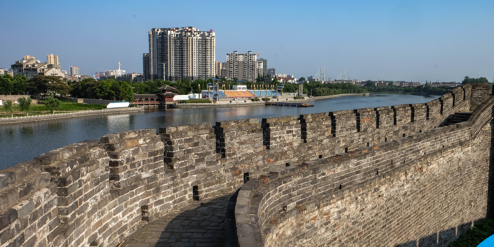 Ancient city wall overlooking a river with modern high rise buildings and a clear blue sky in Jingzhou, China.