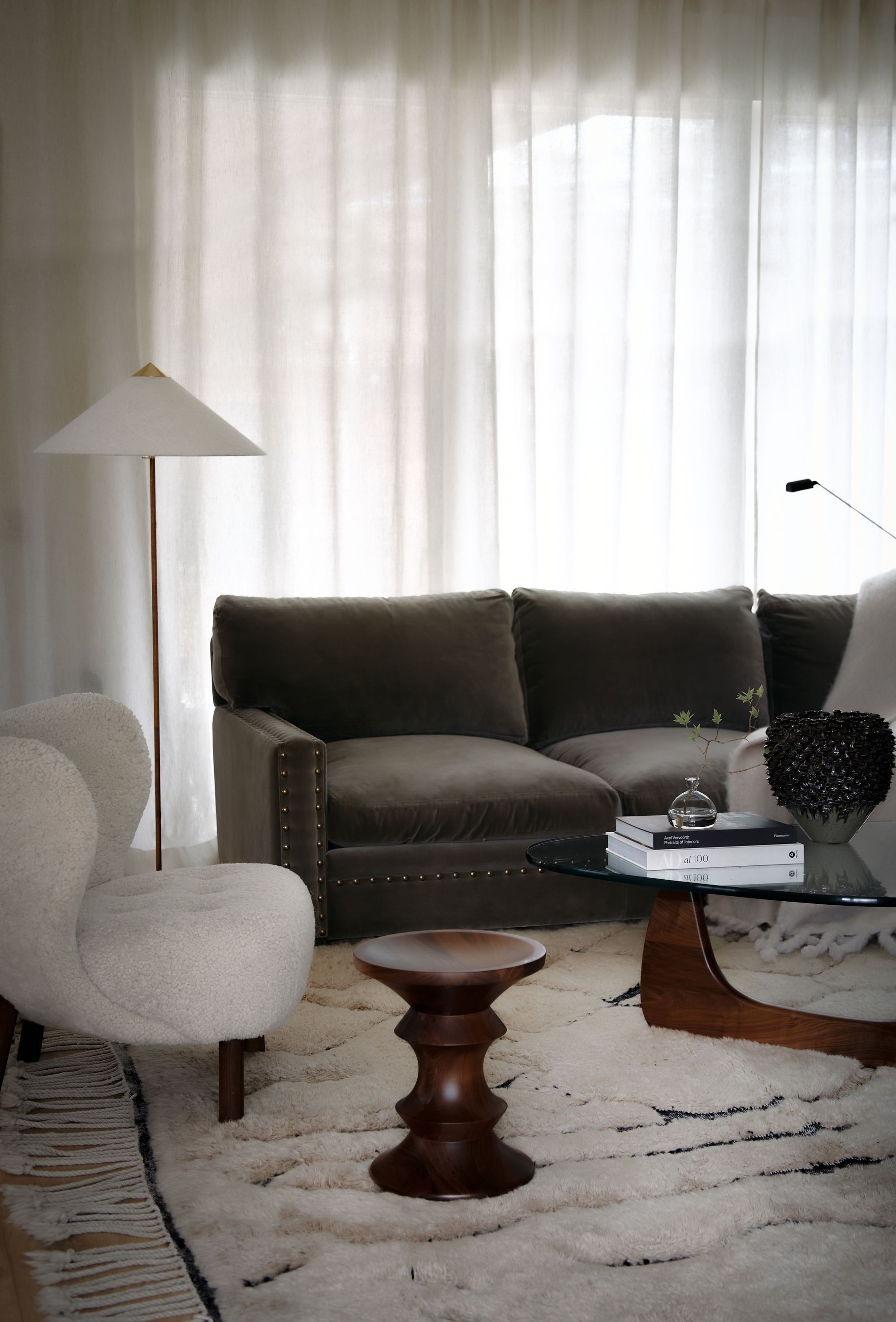 Sober grön soffa. Vit rundad fåtölj. Lampa med vit skärm och vackert glasbord med trä underrede.