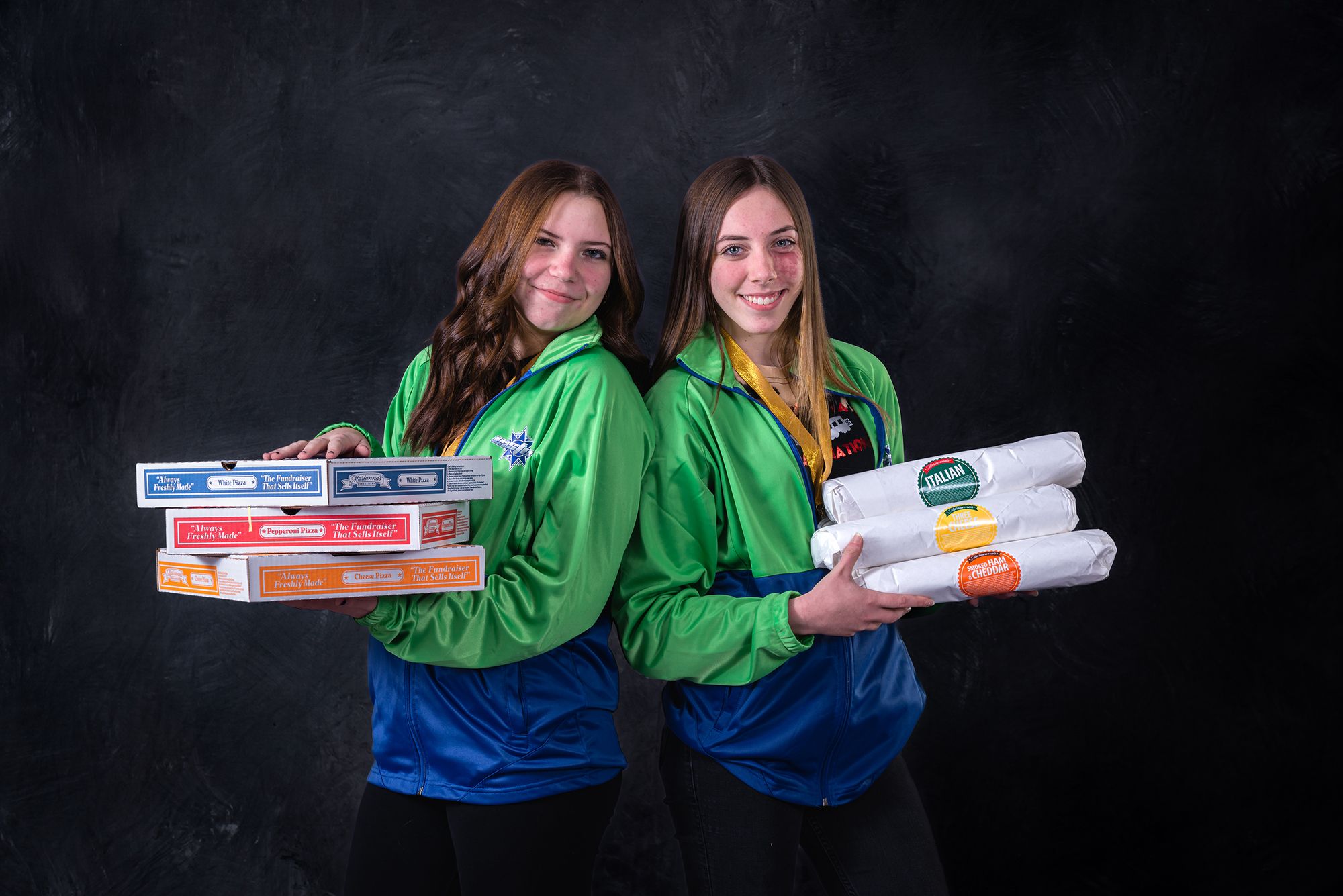 two young women in green and blue sports jerseys holding pizza boxes and wrapped hoagies