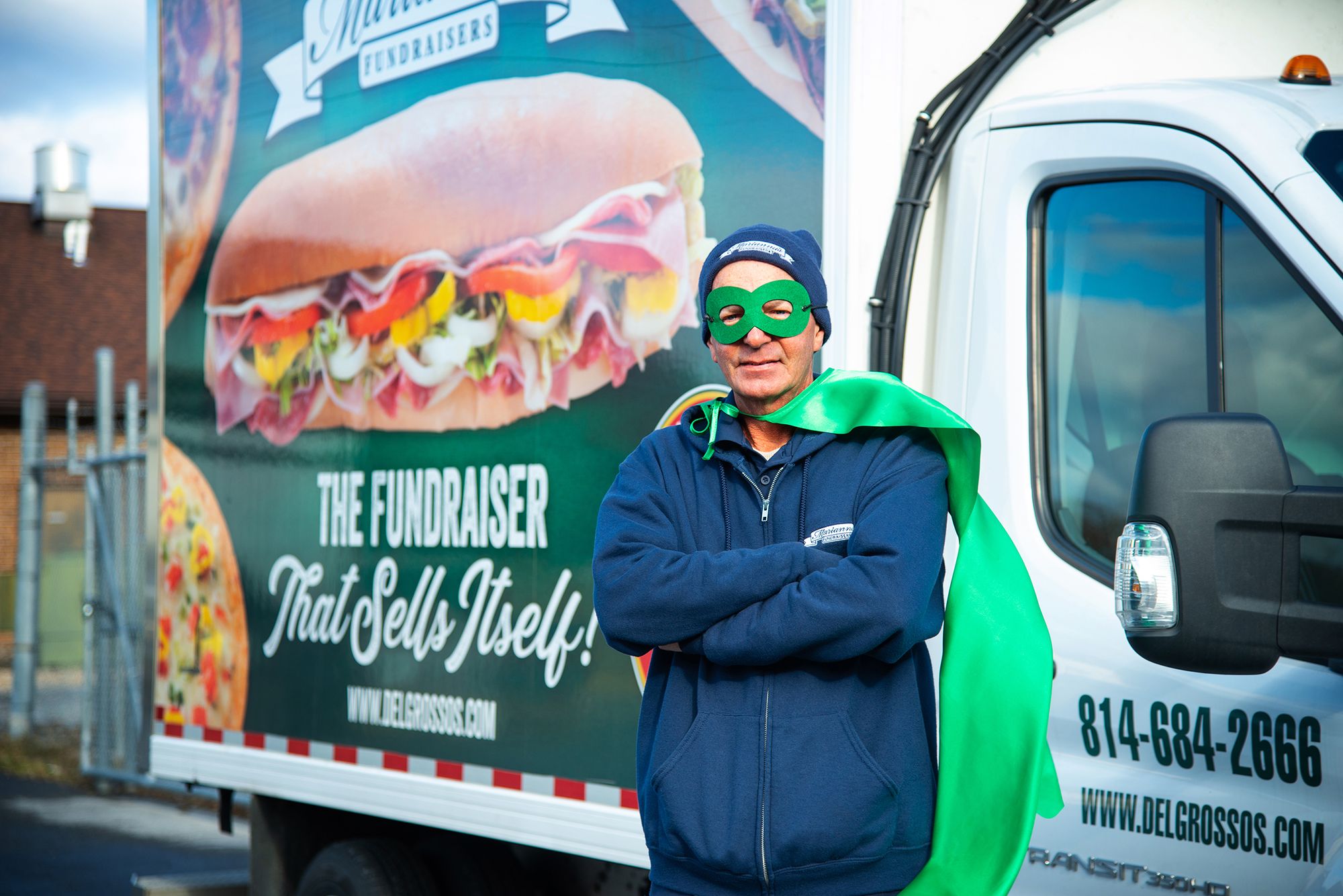 Delivery Employe posing with green cape in front of delivery truck