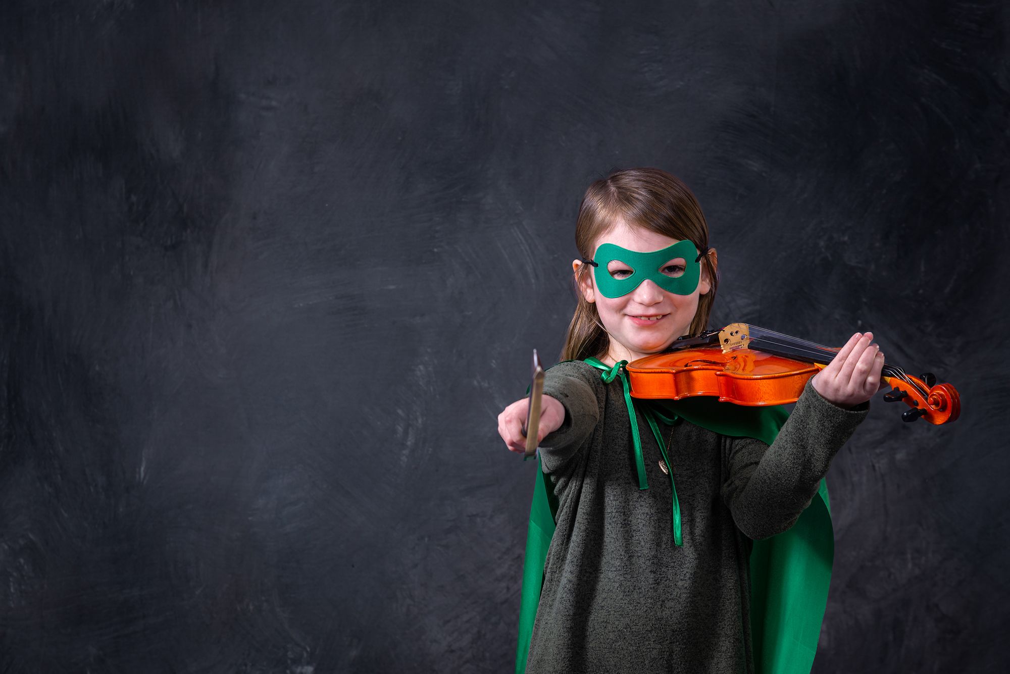 smiling young girl playing the violin, sporting the green hoagie hero cape