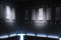 A black and white banner of Marilyn Monroe as well as an all gray banner are hung up in a back and forth pattern by thing cables and rods all around the two walls of a black room.