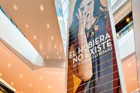 Bottom up view of a large tall paneled wall with an image of a woman covering her face with text "El Hubiera No Existe, no te pierdas las rebajas" printed over.