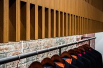 Wooden Fortina panels are lined up vertically above a brick wall with a black pole running horizontally across showcasing black suit jackets on hangers. A large wooden beam runs horizontally through the Fortina panels.