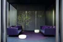 Interior of an elegant space furnished with purple couches, white circular stands, and a plant in a vase. Fortina panels are propped up along the edges of the space.