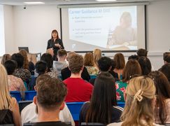 A woman presents a career guidance session to a seated audience in a classroom, with a slide displayed on a screen behind her.
