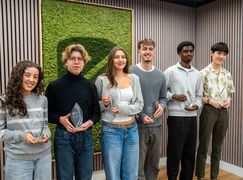 Students holding awards in front of moss mural