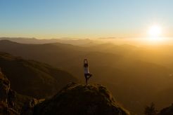 A person stands atop a mountain doing yoga