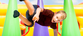 A boy joyfully jumps between colorful inflatable cones at an amusement park, expression filled with excitement and playfulness.