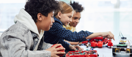 Three children build and interact with electronic robots on a table, focusing intently on their project in a brightly lit room.