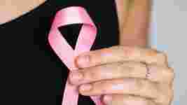 A woman's hand holding a pink breast cancer ribbon