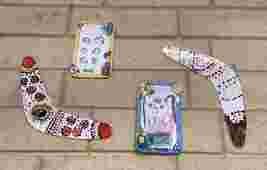 Handmade boomerangs and portraits with colorful patterns and drawings, displayed on a tiled surface.