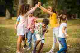 Children play a group game outdoors, laughing and holding hands in a circle on a grassy field.