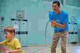 Child playing with a hula hoop in a sports hall with JAG staff in the background