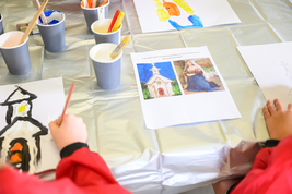 Children painting at a table with cups of paint and a reference sheet showing images of a church and a woman.