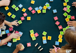 Children's hands playing with colorful alphabet and number blocks on a dark green surface.