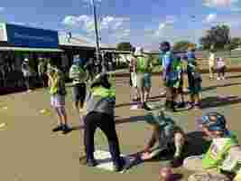 Children playing lawn bowls outside the Thornlie Bowling Club, interacting and wearing colorful hats under a sunny sky.