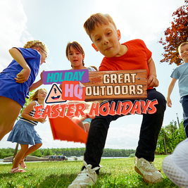 Children playing outdoors on a sunny day near a lake. Text overlay reads "Holiday HQ The Great Outdoors Easter Holidays."