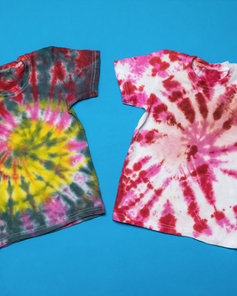 Two tie-dye T-shirts on a blue background, one with yellow and dark colors, the other in red and pink patterns.