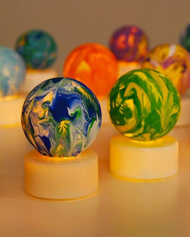 Colorful, marbled glass orbs on glowing bases in warm lighting, featuring swirls of blue, green, and orange.