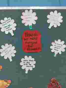 Bulletin board with paper flowers sharing ideas on inclusion, such as being kind and respectful, around a central question: "How do we make everyone feel included?"