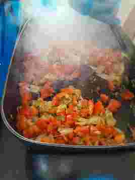 Sizzling chopped tomatoes and onions being stirred in a hot pan, with steam rising visibly.