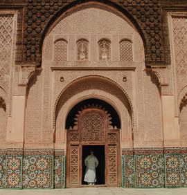 An extremely grand and ornate door with several distinct layers of detail including wood carvings and tile work with a man standing in the middle of the entrance