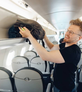 Muž v letadle ukládá batoh do zavazadlového prostoru